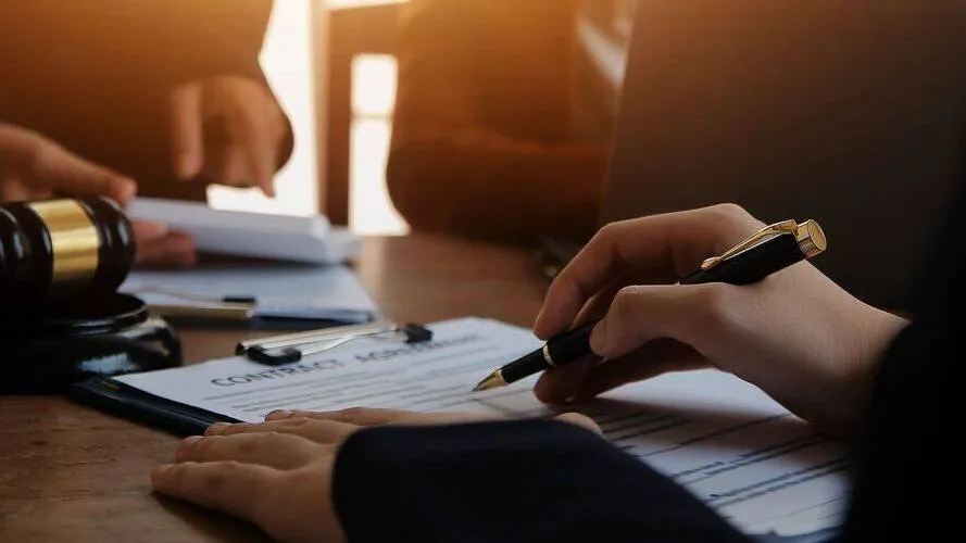 Close-up of hands signing a contract agreement with a pen, gavel on wooden table.