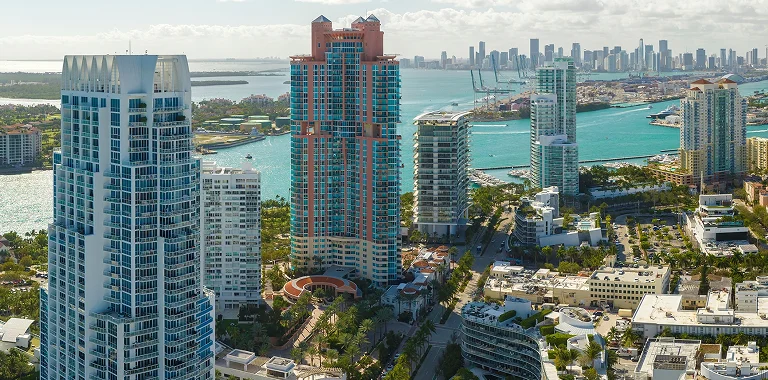 Aerial view of a coastal city with high-rise buildings, turquoise water, and a distant skyline.