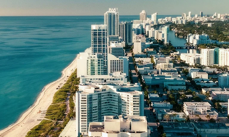 Aerial view of a coastal cityscape with high-rise buildings, sandy beach, and ocean.