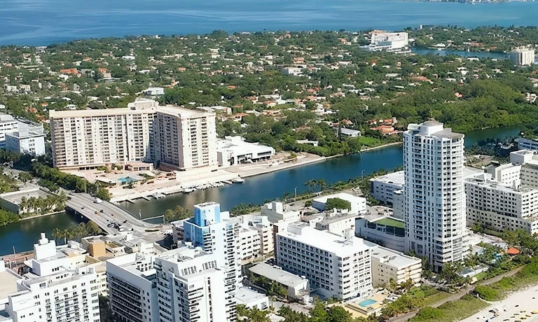 Aerial view of coastal cityscape with high-rise buildings, a waterway, and greenery.