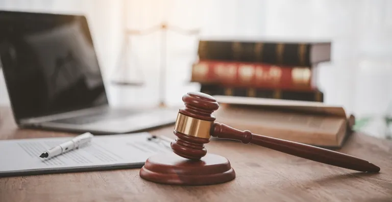 Wooden judge's gavel with legal documents, laptop, and law books on desk.