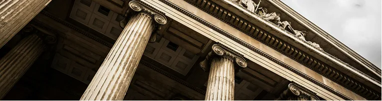 Low-angle view of classical stone columns and sculpted frieze on historic building facade.