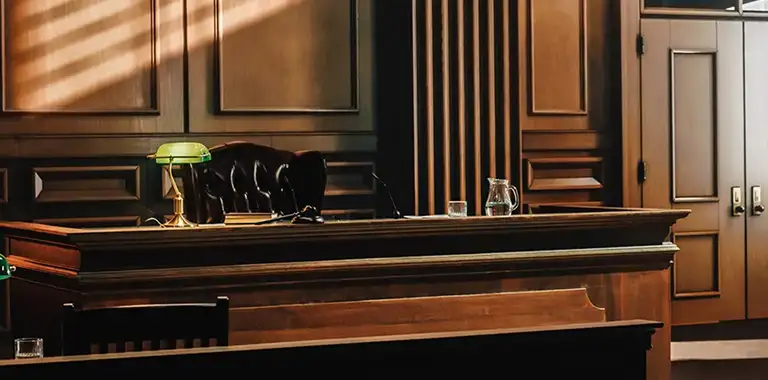 Empty courtroom bench and judge's desk with green lamp and water pitcher.