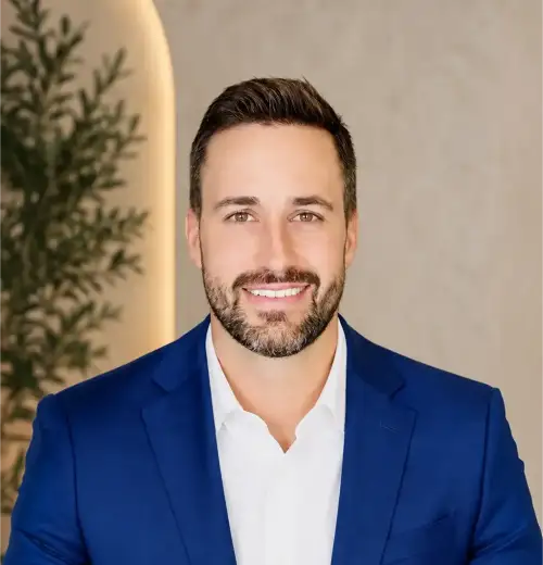 Professional headshot of a smiling man with dark hair and beard, wearing a blue suit and white shirt.