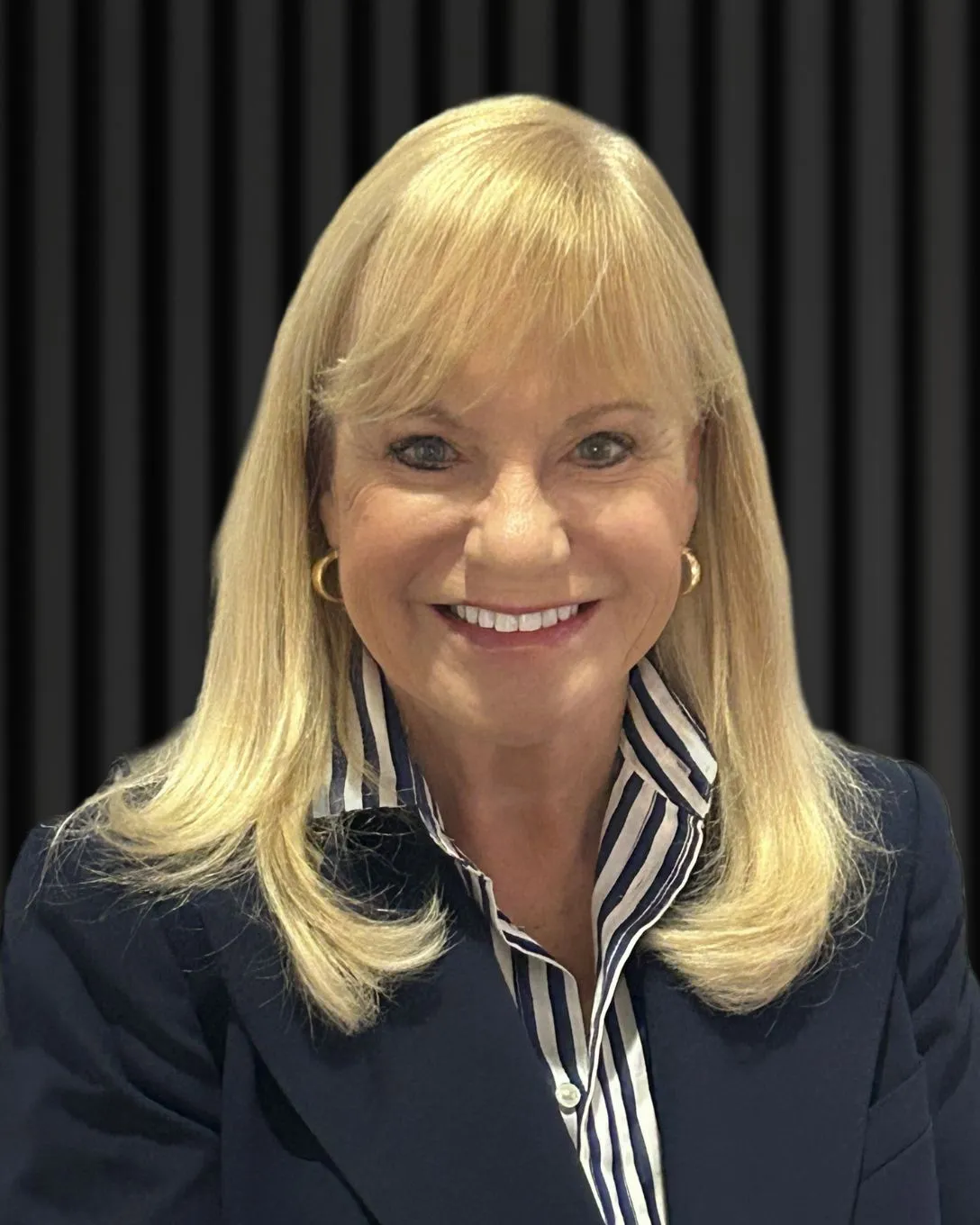 Professional portrait of a smiling blonde woman in a navy blazer and striped shirt - Lyne Ranson